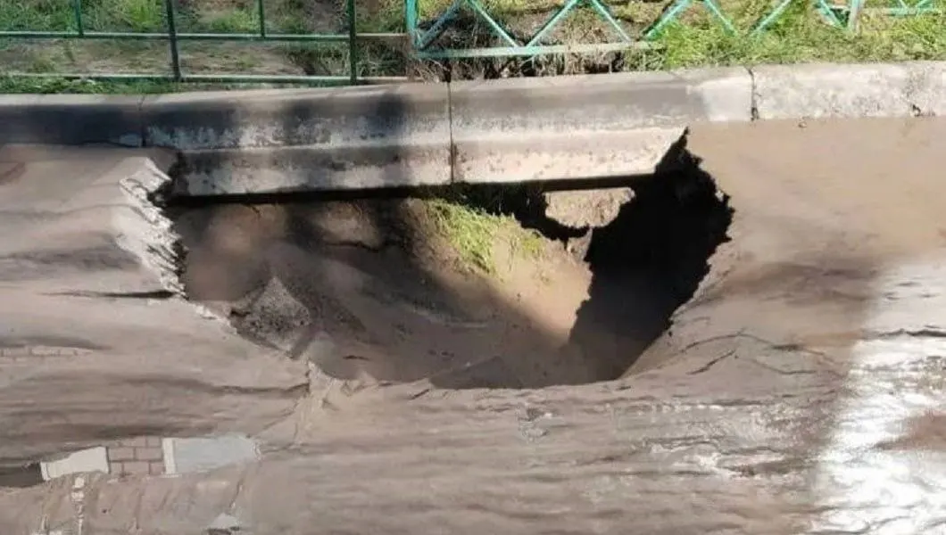 Из-за прорыва вода заливает дорогу и тротуары, жильцы обходят лужи, а ремонт идёт по приоритету.